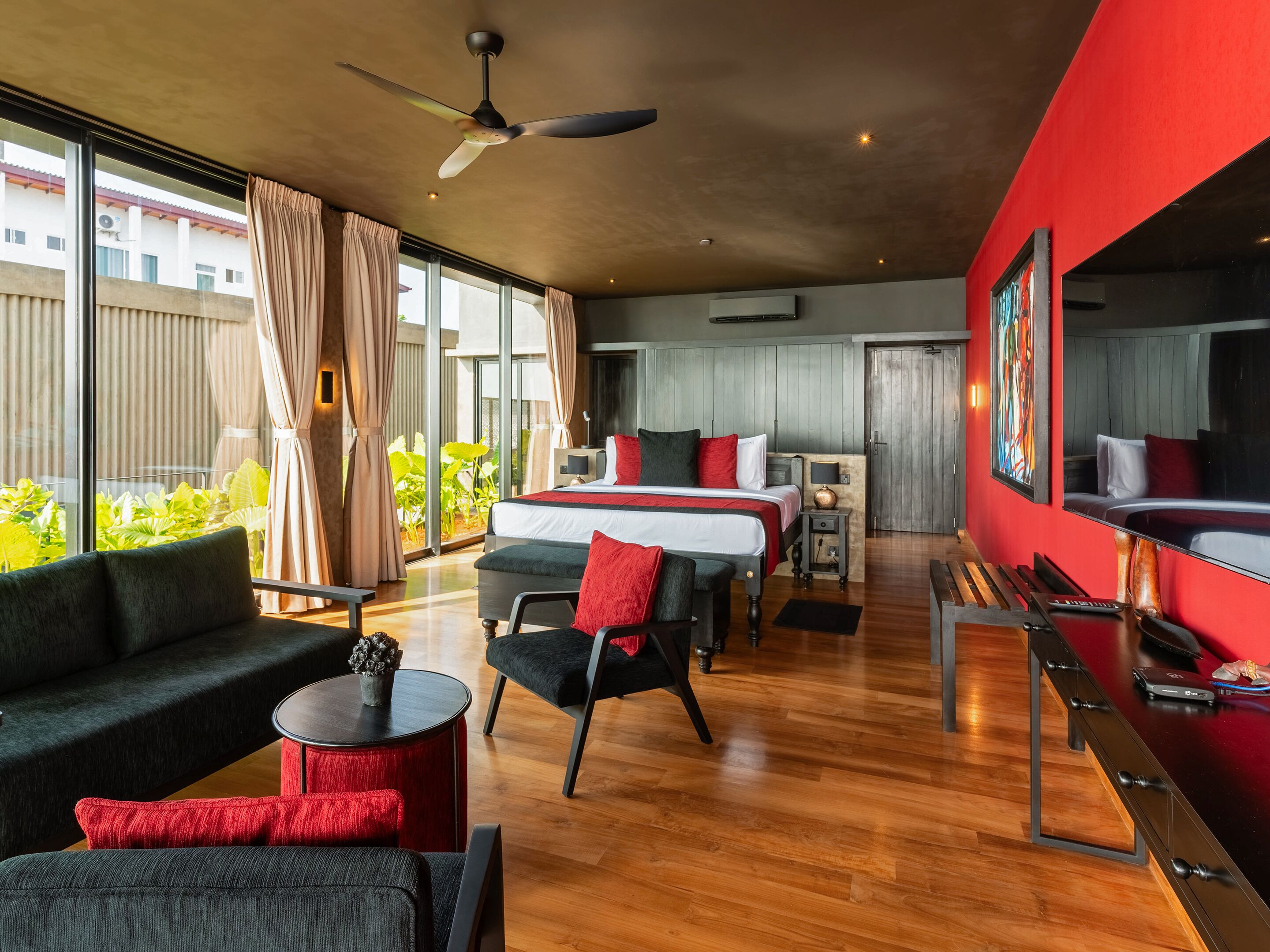 A modern hotel room with a large bed, a sofa, a desk, and a ceiling fan.