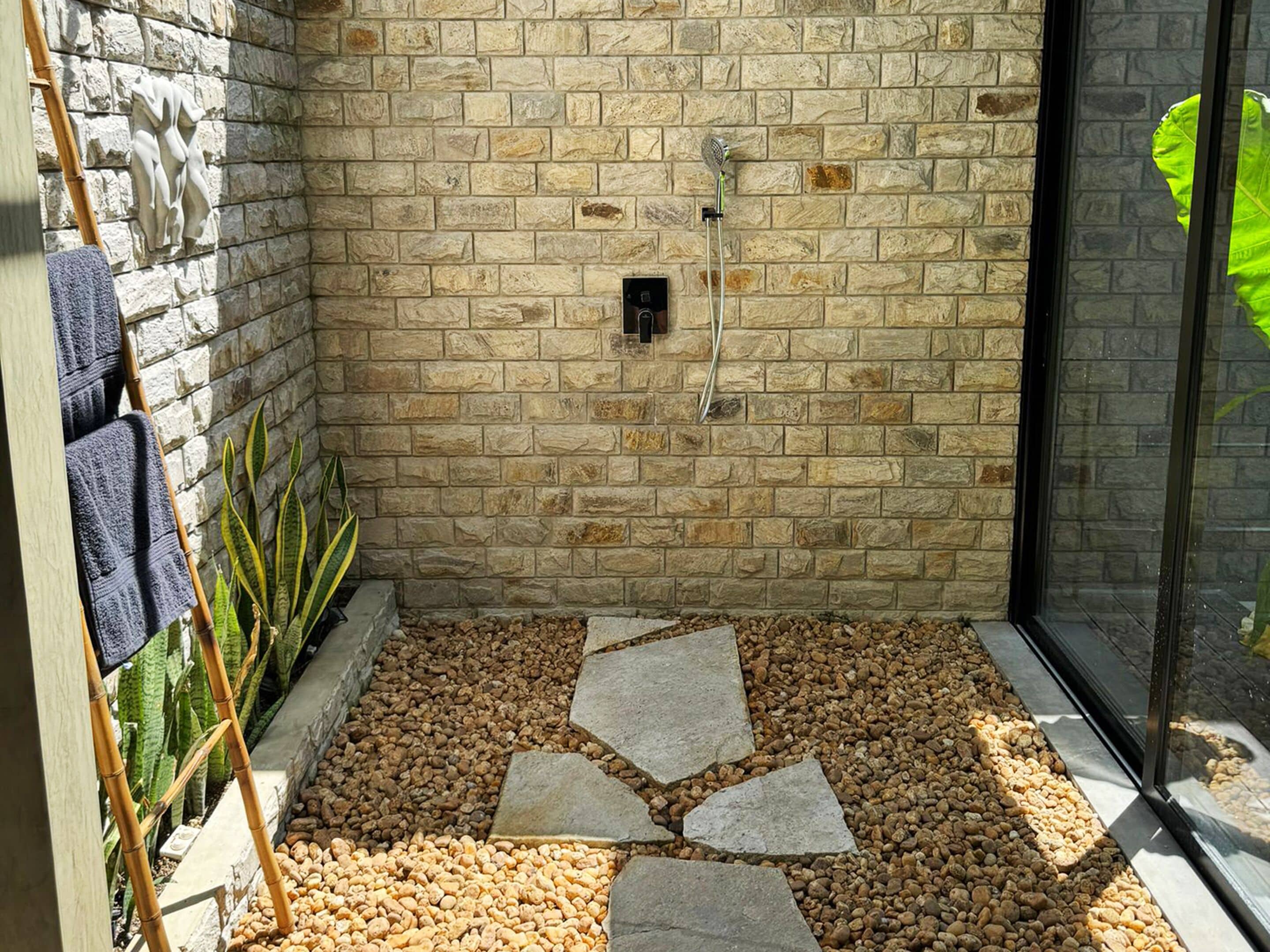 A stone-walled shower area with a pebble floor and a glass door.