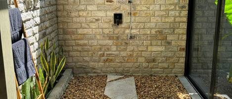 A stone-walled shower area with a pebble floor and a glass door.
