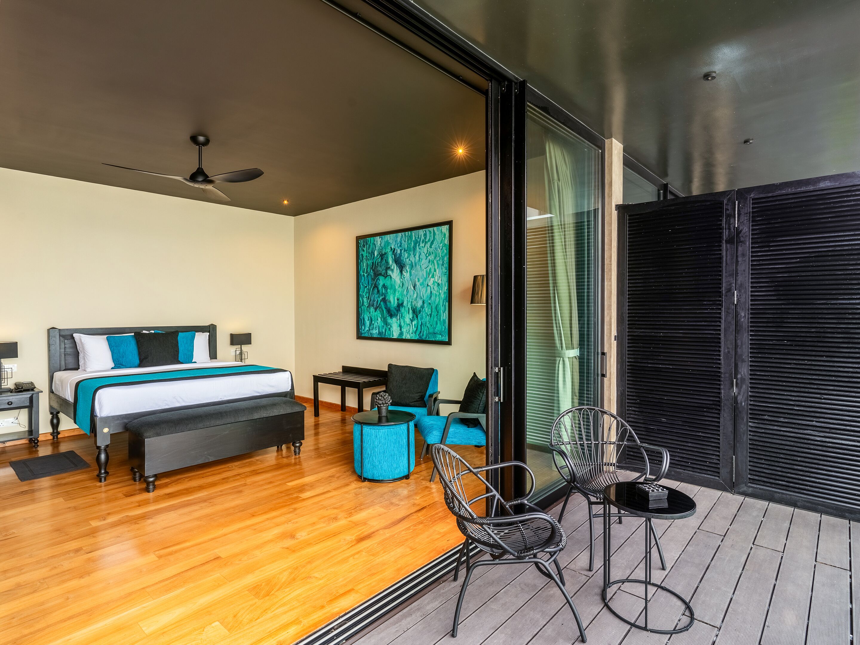 A modern hotel room with a large bed, a desk, and a balcony with chairs.