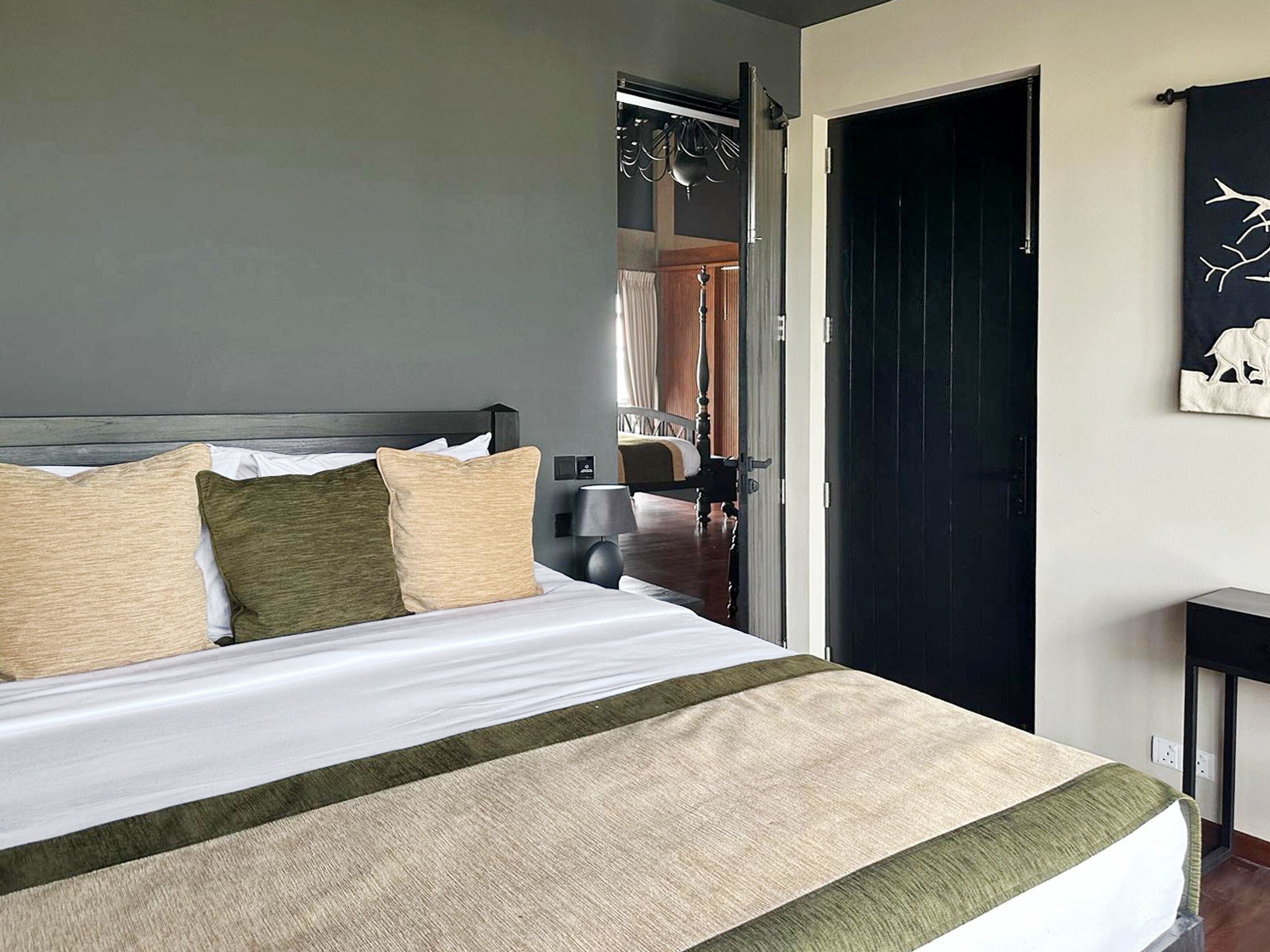 A bedroom with a bed, a bedside table, a door, and a wall with a painting.