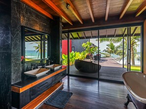 Ein modernes Badezimmer mit einem großen Spiegel, zwei Waschbecken, einer Badewanne und Meerblick.
