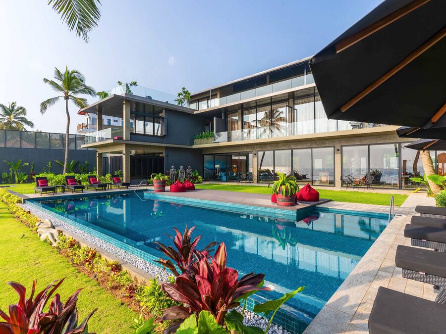 A modern hotel with a large outdoor swimming pool, multiple lounge areas, and a well-maintained garden.