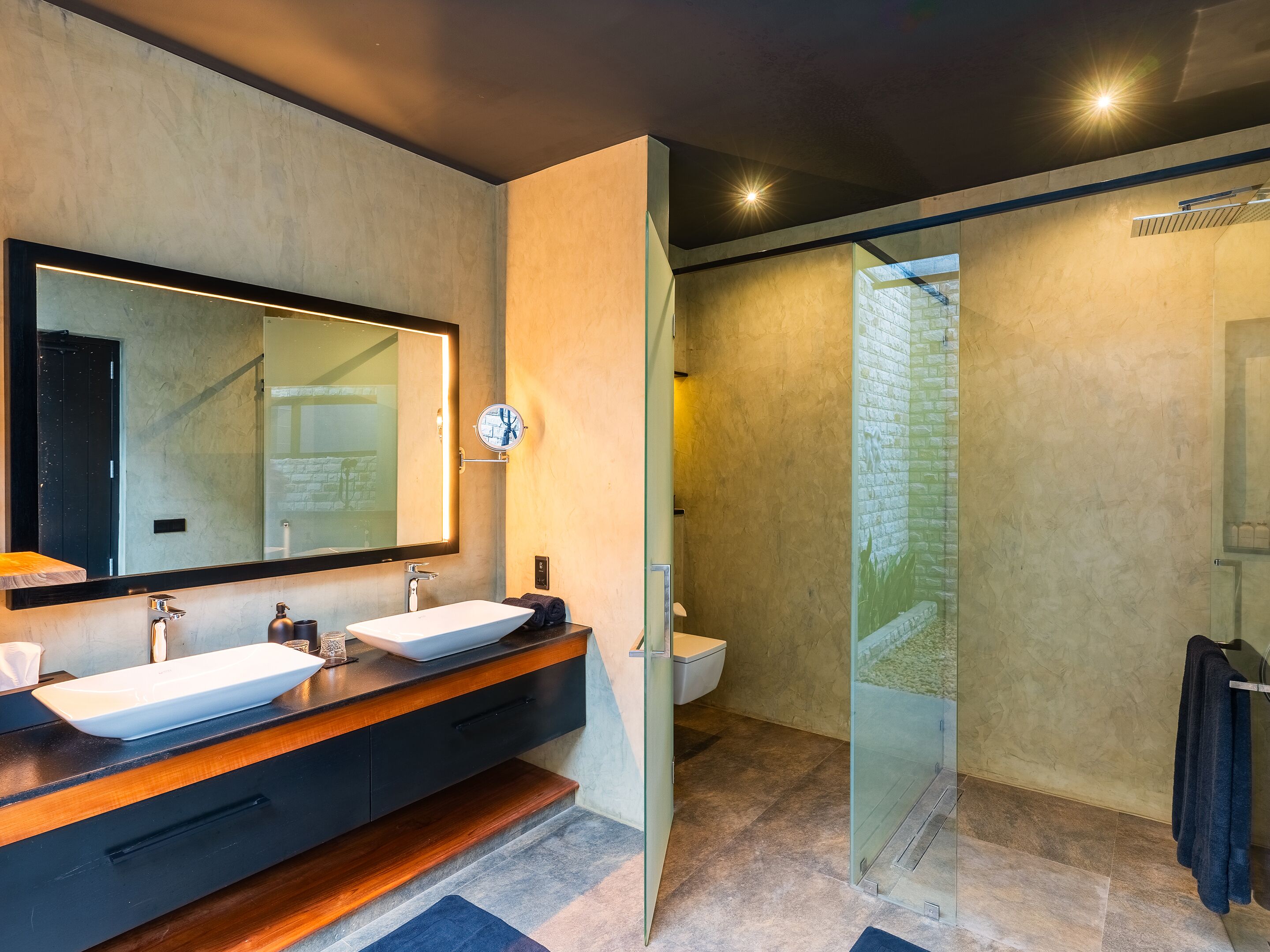A modern bathroom with a large mirror, two sinks, a glass shower enclosure, and a wooden vanity.