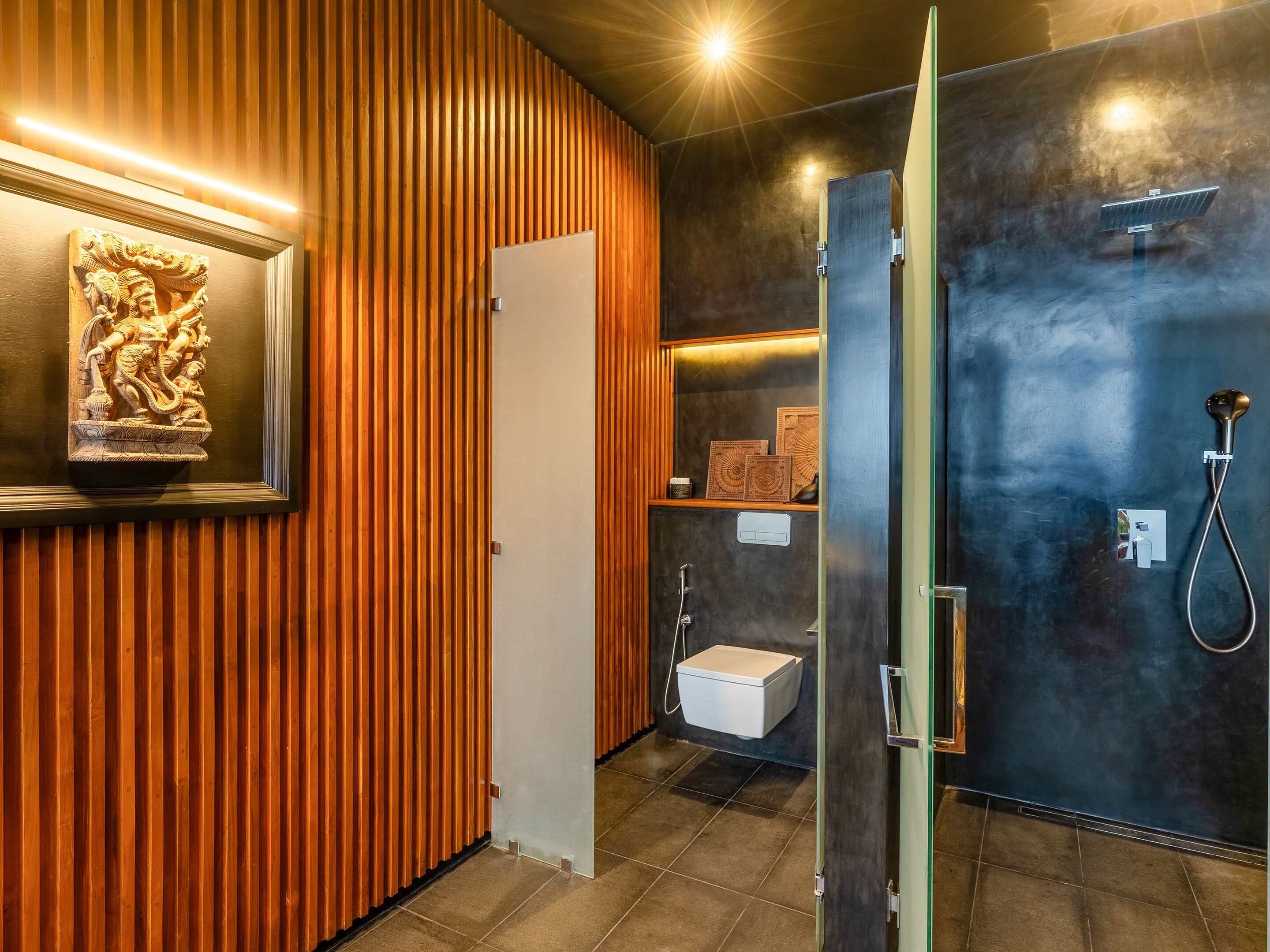 A modern bathroom with a wooden panel wall, a framed sculpture, a shower area, and a toilet.