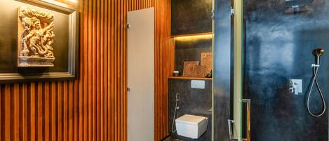 A modern bathroom with a wooden panel wall, a framed sculpture, a shower area, and a toilet.