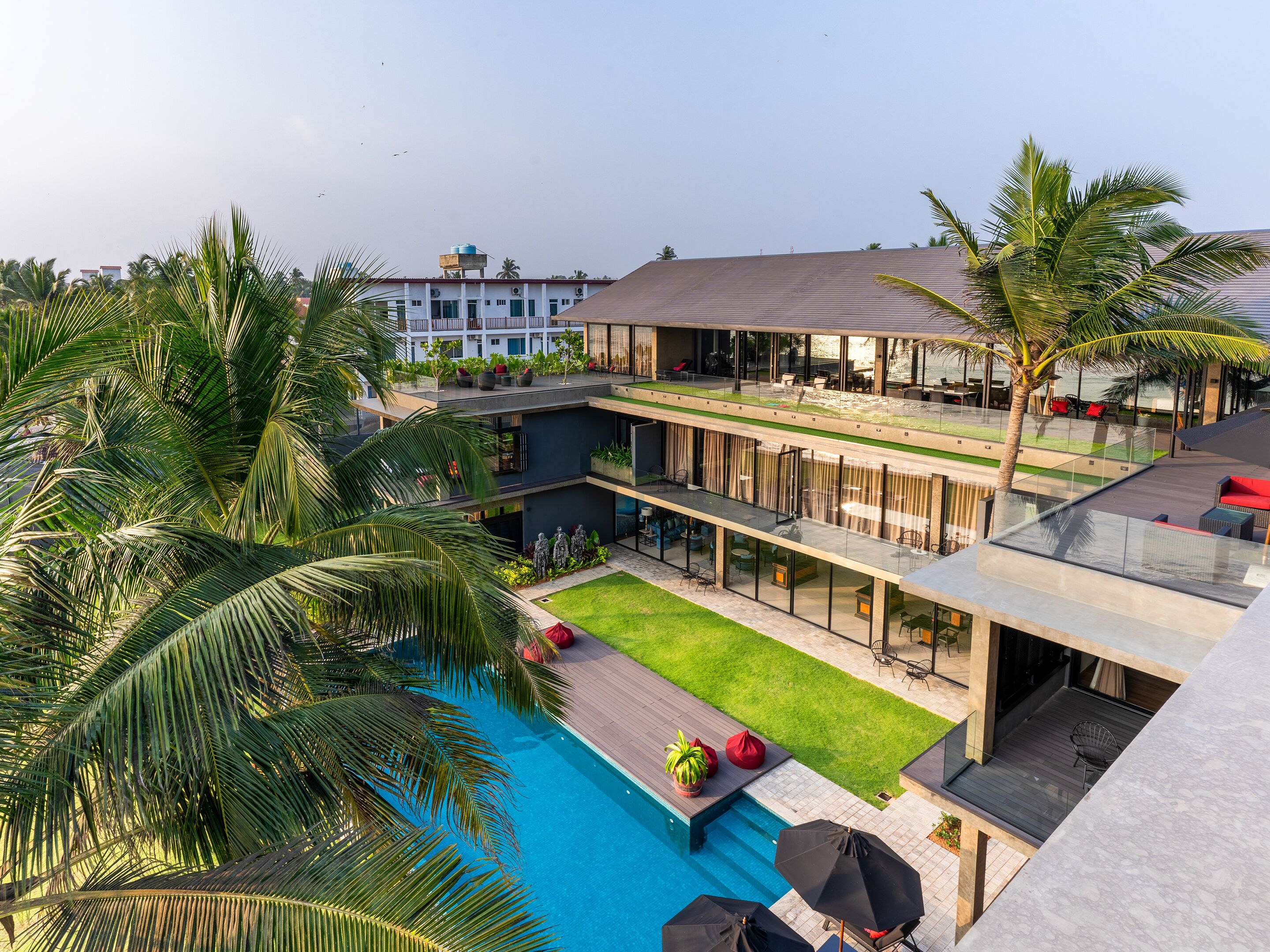 A modern hotel with a rooftop pool, outdoor seating, and lush greenery.