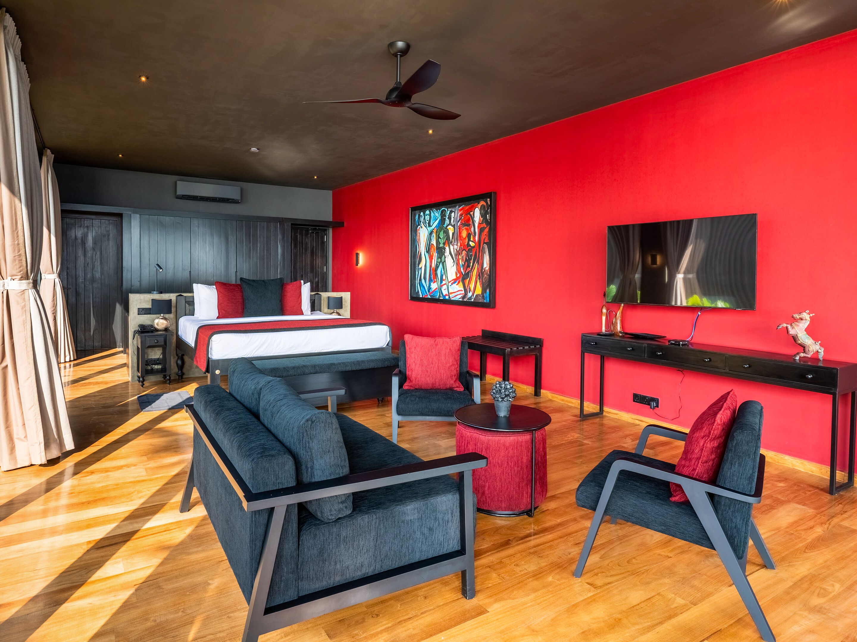 Une chambre d’hôtel moderne avec un mur d’accent rouge, un grand lit, un canapé, une table basse et un téléviseur.