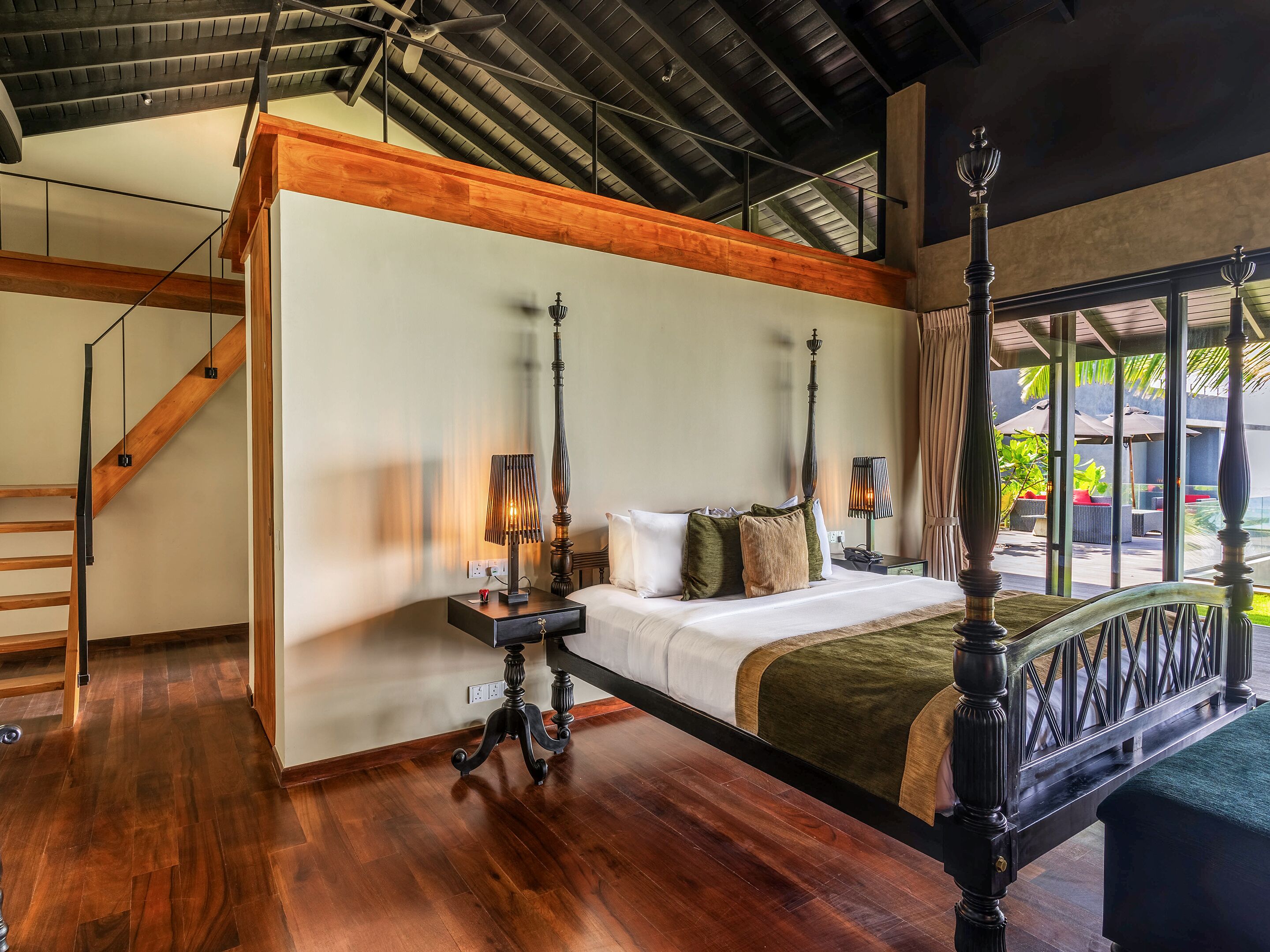 A bedroom with a four-poster bed, wooden beams, a staircase, and a view of the outdoors.