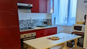A compact kitchen with red cabinets, a white countertop, and a tiled backsplash.