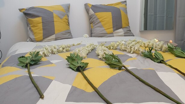 A neatly made bed with a geometric patterned bedspread, two pillows with a yellow and gray design, and a garland of white flowers on the bed.