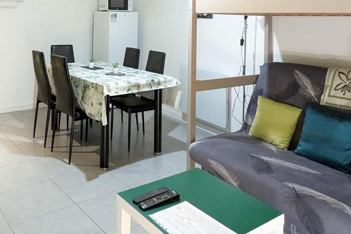 Een compact woongedeelte met een eethoek, een bank met decoratieve kussens en een bijzettafeltje met een afstandsbediening.