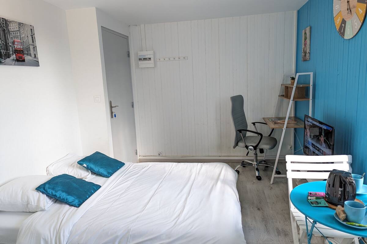 Hotelkamer met een bed, bureau, stoel, klok en een klein tafeltje met een beker en tas.
