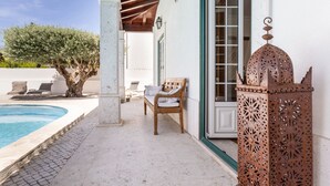 A poolside area with a wooden bench, a metal lantern, and a white building with a green door. - Casa Das Azeitonas (Azeitão)