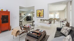 A spacious living room with a modern sofa, a coffee table, and a red cabinet. There is a dining area with a table and chairs in the background. - Casa Branca - Magnificent villa with private pool (Aroeira)