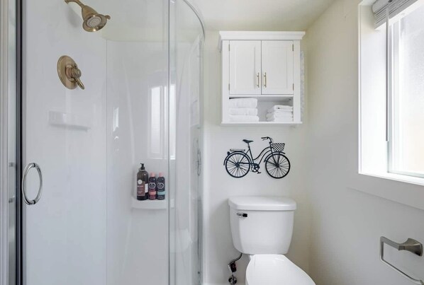 Un baño moderno con cabina de ducha de vidrio, inodoro y un armario blanco sobre el inodoro.