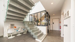 A modern interior with a glass staircase, white chairs, and a visible fire extinguisher. - Casa Nilo Design - Villa with pool near the beach (Aroeira)