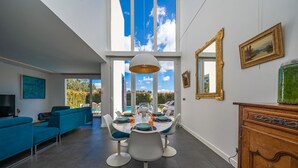 A modern dining area with a large table, blue chairs, and a view of the sky through large windows. - Casa Nilo Design - Villa with pool near the beach (Aroeira)