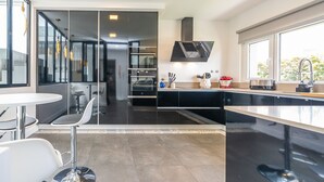 A modern kitchen with a black countertop, stainless steel appliances, and a window providing natural light. - Casa Nilo Design - Villa with pool near the beach (Aroeira)