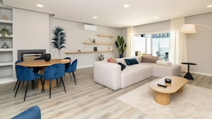 Un salon moderne comprenant un coin repas, un canapé blanc, des fauteuils bleus et une table basse en bois.