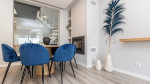 Un salon moderne avec un coin repas, comprenant un escalier, une grande plante en pot et une étagère en bois.
