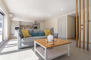 A modern living room with a sofa, a wooden coffee table, and a kitchen in the background.