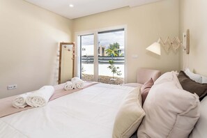 A hotel room with a bed, a window with a view, a wall-mounted lamp, and a towel rack.