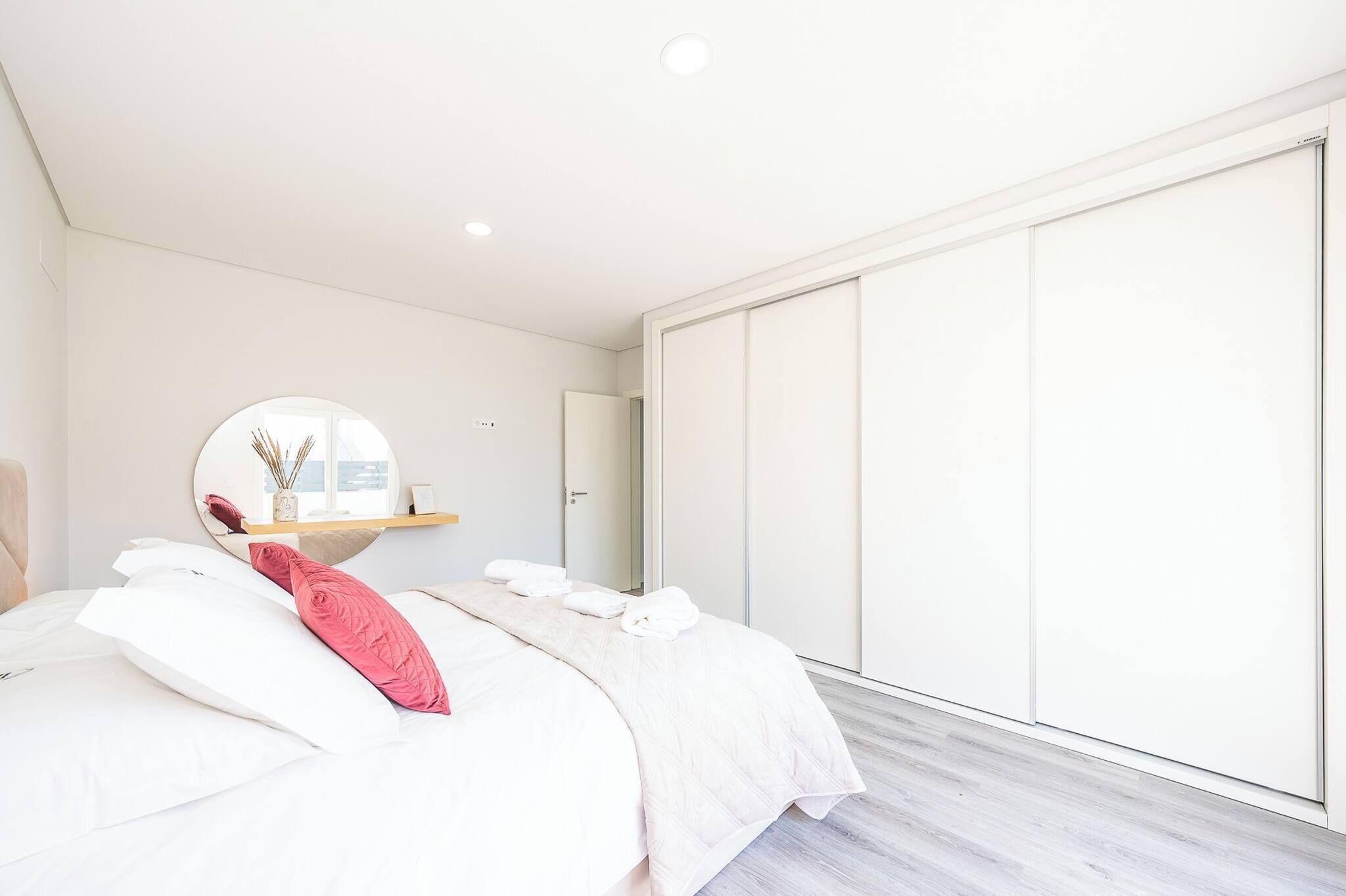 Ein modernes Schlafzimmer mit einem großen Bett, einem runden Spiegel, einem Kleiderschrank und einem Fenster.