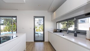 Une cuisine moderne avec des meubles blancs, un plan de travail noir et une vue sur un patio aménagé avec du mobilier d’extérieur.