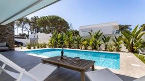Un espace piscine avec une table en bois et des chaises longues blanches.