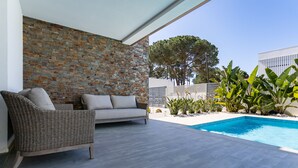 Une terrasse extérieure moderne, agrémentée d’un mur en pierre, d’une piscine et d’un canapé en osier.