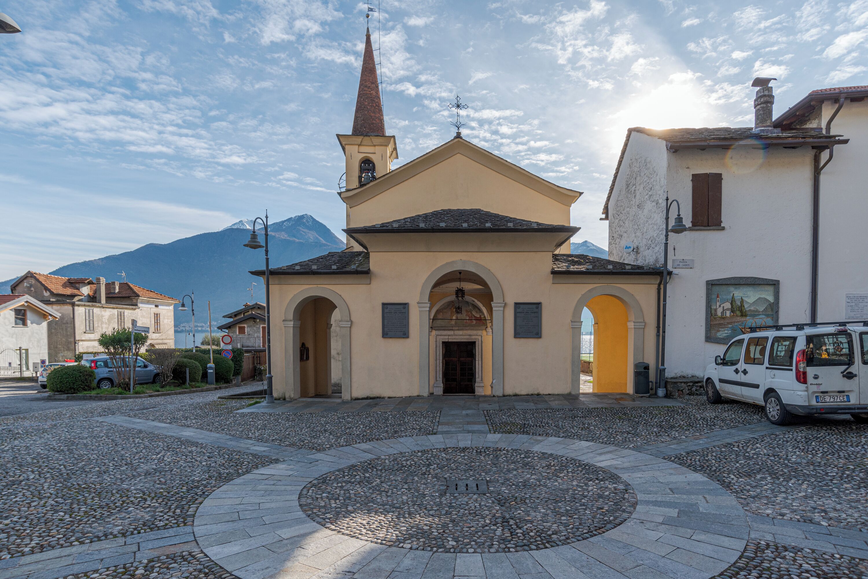 A church with a bell tower, a circular stone pavement, and a mountain in the background.