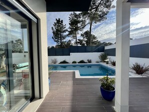 A modern outdoor pool area with a clear view of the sky, surrounded by a wooden deck and potted plants.