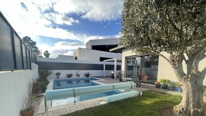 A modern outdoor pool area with a glass enclosure, surrounded by a well-maintained lawn and potted plants. - Casa Marido - Villa with swimming pool (Pinhal do Cabedal)