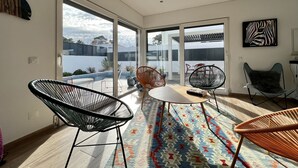 A modern living room with a large glass door leading to a balcony, a round table, and two chairs. - Casa Marido - Villa with swimming pool (Pinhal do Cabedal)