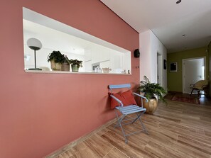A modern interior with a red wall, a large mirror, a blue folding chair, and a wooden floor.