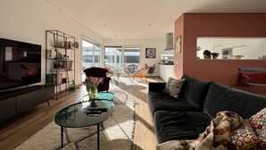 A modern living room with a flat-screen TV, a glass coffee table, and a sofa. There is a dining area with chairs and a table, and a kitchen in the background. - Casa Marido - Villa with swimming pool (Pinhal do Cabedal)