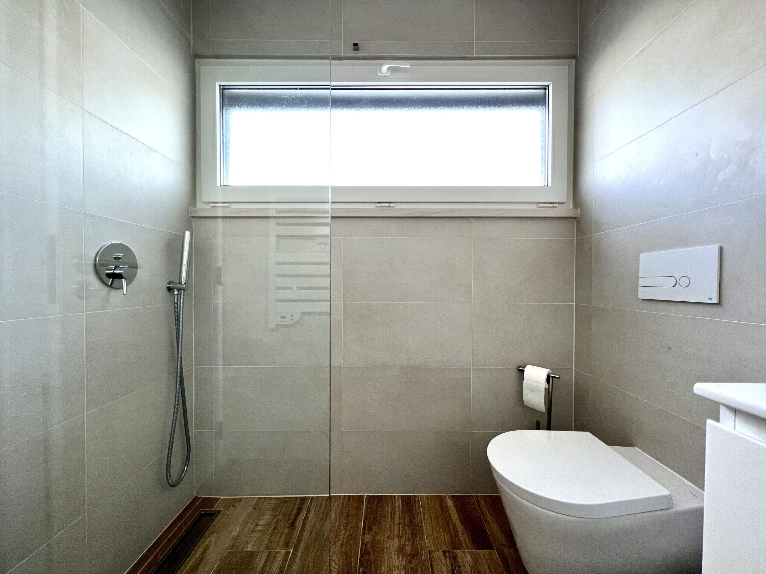 A modern bathroom with a shower, toilet, and a window.