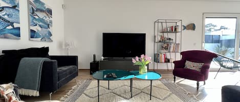 A modern living room with a flat-screen TV, a sofa, a coffee table, and a bookshelf.