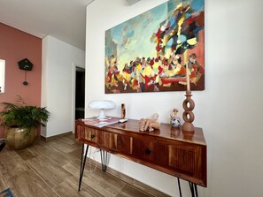 Un salon moderne avec une console en bois, une grande peinture abstraite, une plante en pot et une horloge au mur.