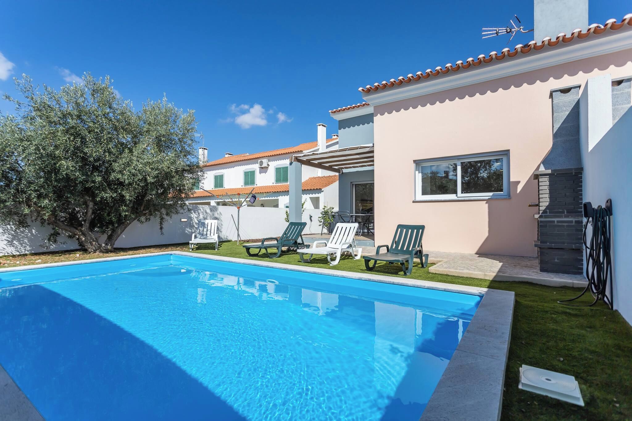 A swimming pool with lounge chairs, a white building with a tiled roof, and a tree.