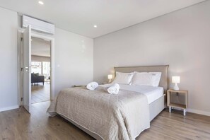 A modern bedroom with a large bed, bedside lamps, and a visible door leading to another room.