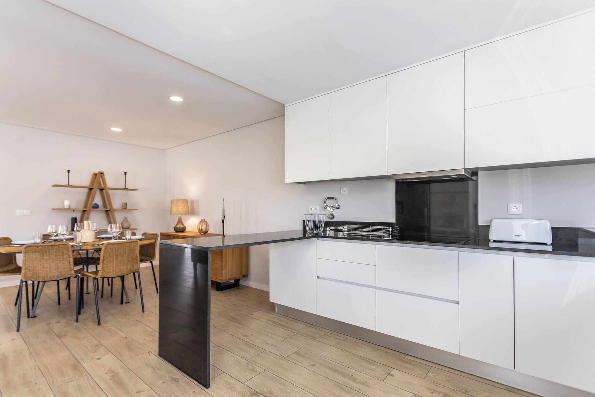 A modern kitchen with white cabinets, a black countertop, and a dining area with wicker chairs and a wooden table.