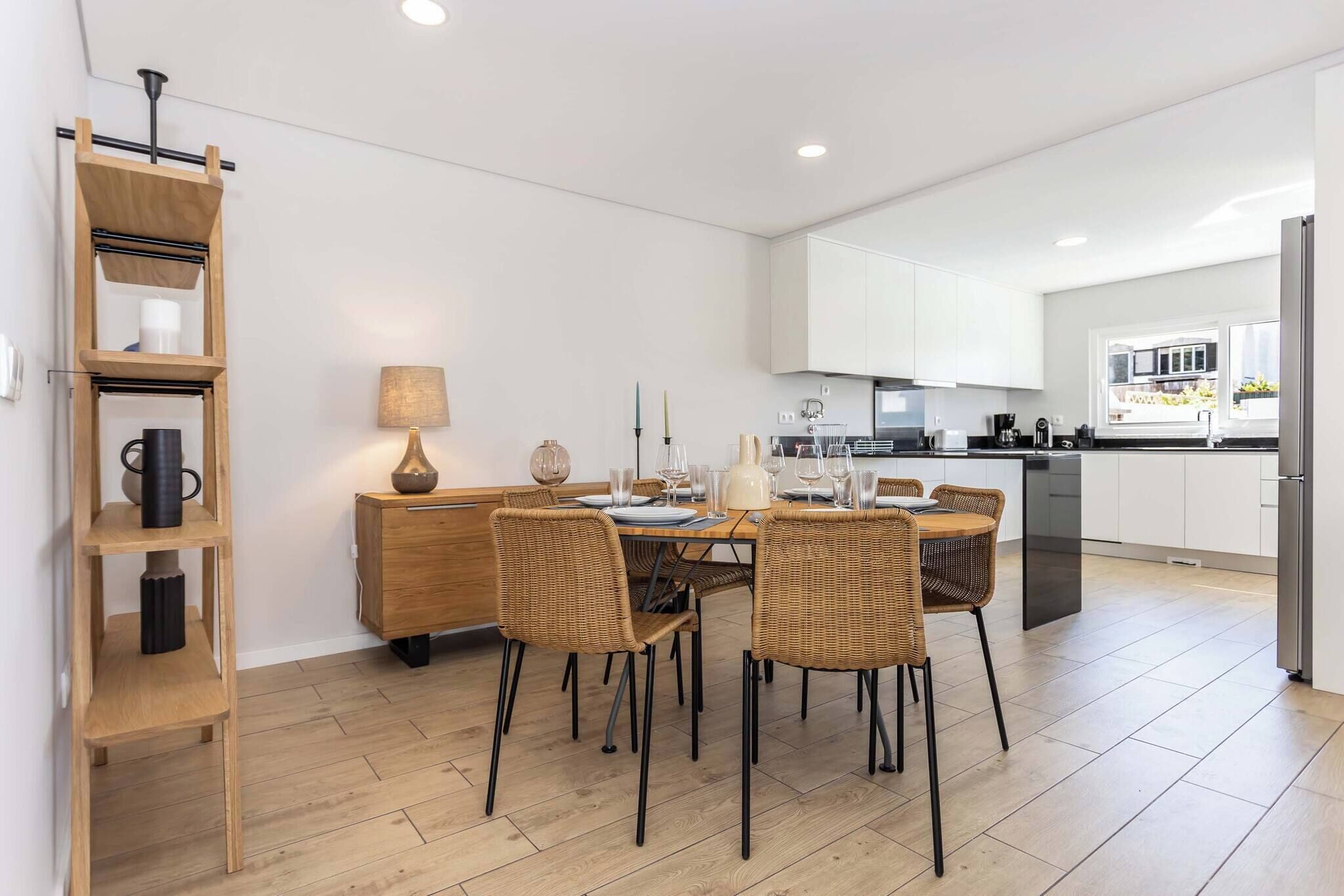 A modern kitchen with white cabinets, a dining area with wicker chairs, and a wooden shelf unit.