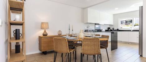 A modern kitchen with white cabinets, a dining area with wicker chairs, and a wooden shelf unit.