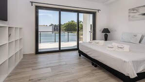 Une chambre moderne dotée d’un grand lit, d’une porte-fenêtre coulissante donnant sur un balcon et d’un téléviseur à écran plat fixé au mur.
