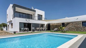Une maison moderne à deux étages, dotée d’une piscine, d’un espace extérieur aménagé et d’un mur en pierre.