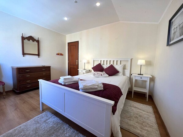 A bedroom with a bed, bedside tables, a dresser, a mirror, and a door.