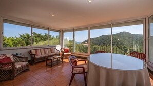 A spacious balcony with a table and chairs, large windows offering a view of a mountainous landscape. - Casa D'Aroeira - Serra d'Arrabida (Azeitão)