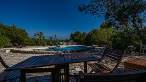 A pool area with lounge chairs and a table, surrounded by stone walls and greenery. - Casa D'Aroeira - Serra d'Arrabida (Azeitão)